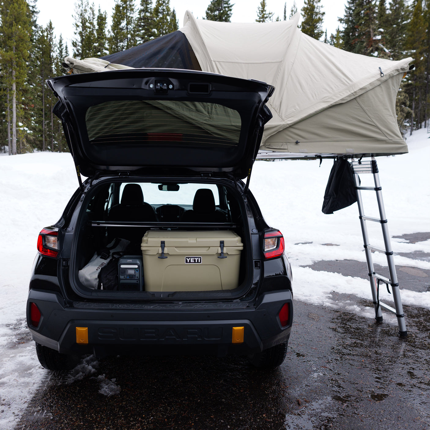 Subaru with rooftop tent deployed, YETI cooler, & Anker power station for snowy car camping. RV rental alternative.