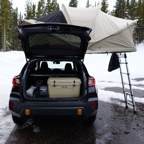 Subaru with rooftop tent deployed, YETI cooler, & Anker power station for snowy car camping. RV rental alternative.