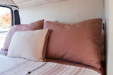Comfortable RV rental interior featuring a cozy bed with blush and white pillows, ideal for van life.