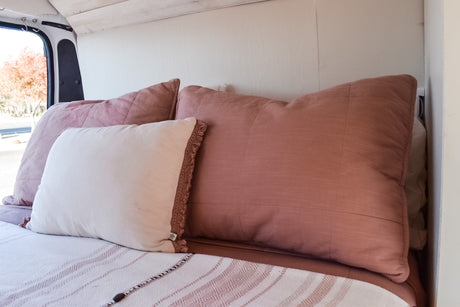 Comfortable RV rental interior featuring a cozy bed with blush and white pillows, ideal for van life.