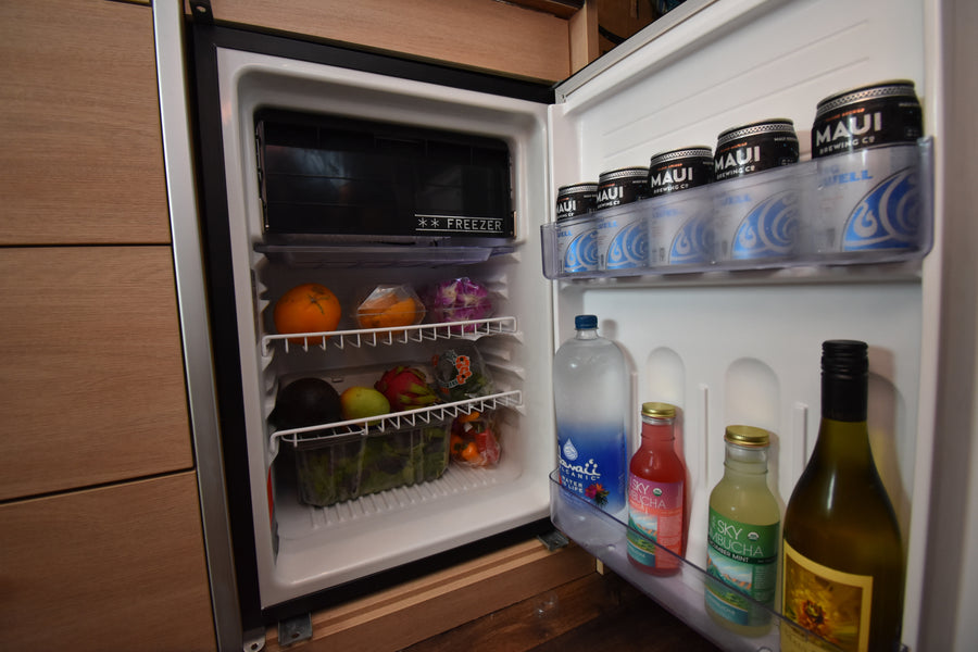 RV rental mini-fridge stocked with Maui beer, kombucha, water, fresh fruits (oranges, dragon fruit), and veggies.