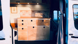 Inside a sleek camper van: custom wood kitchen with drawers, sink, and tiled backsplash. Perfect for your next RV rental.