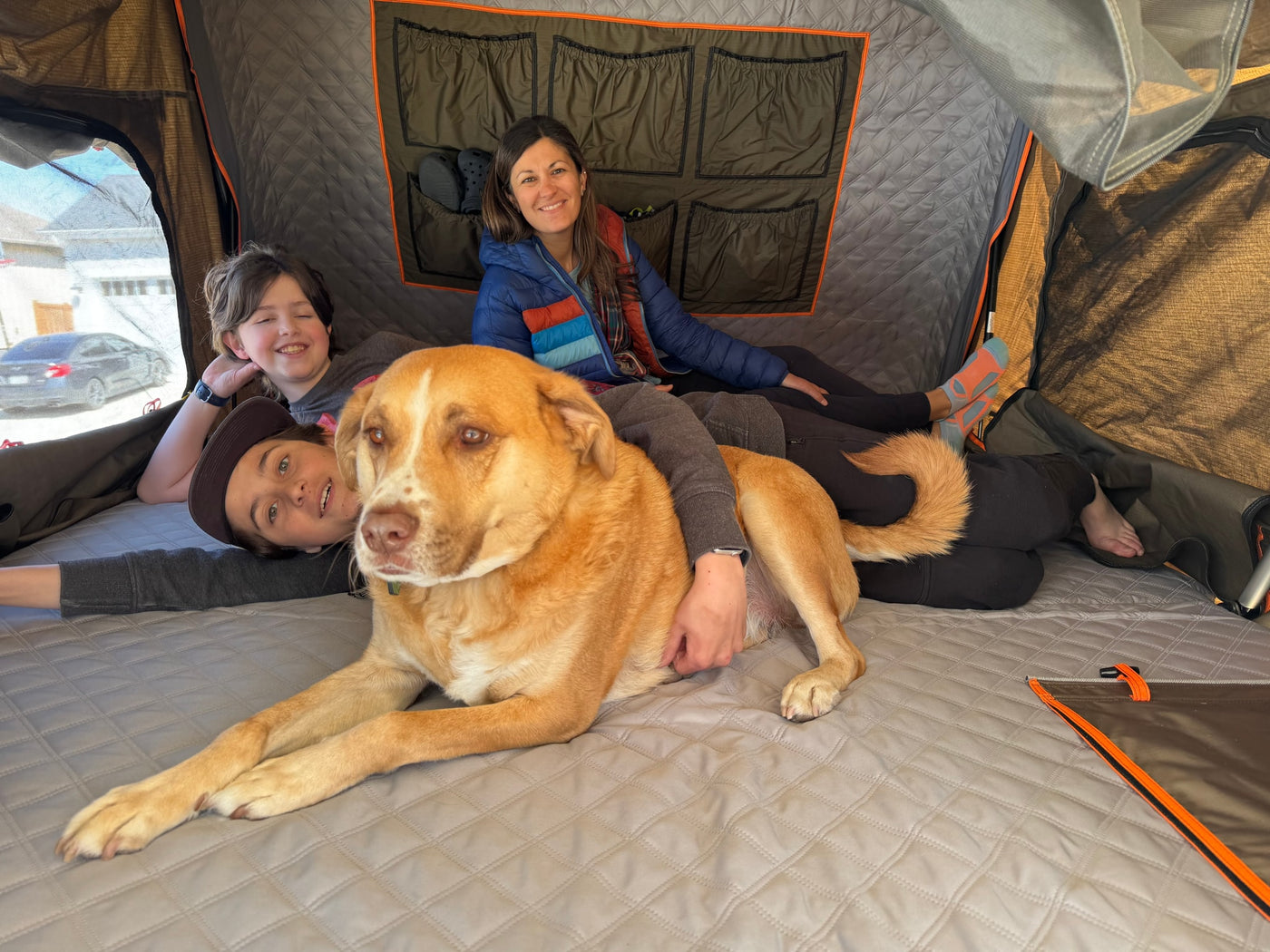 Cozy family fun in an RV rental's rooftop tent. Dog, two kids, and woman relax inside on a quilted mattress. — photo 17