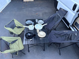 RV rental outdoor dining: foldable table, four chairs (2 green, 2 gray), pots, and dishware set up on pavement.