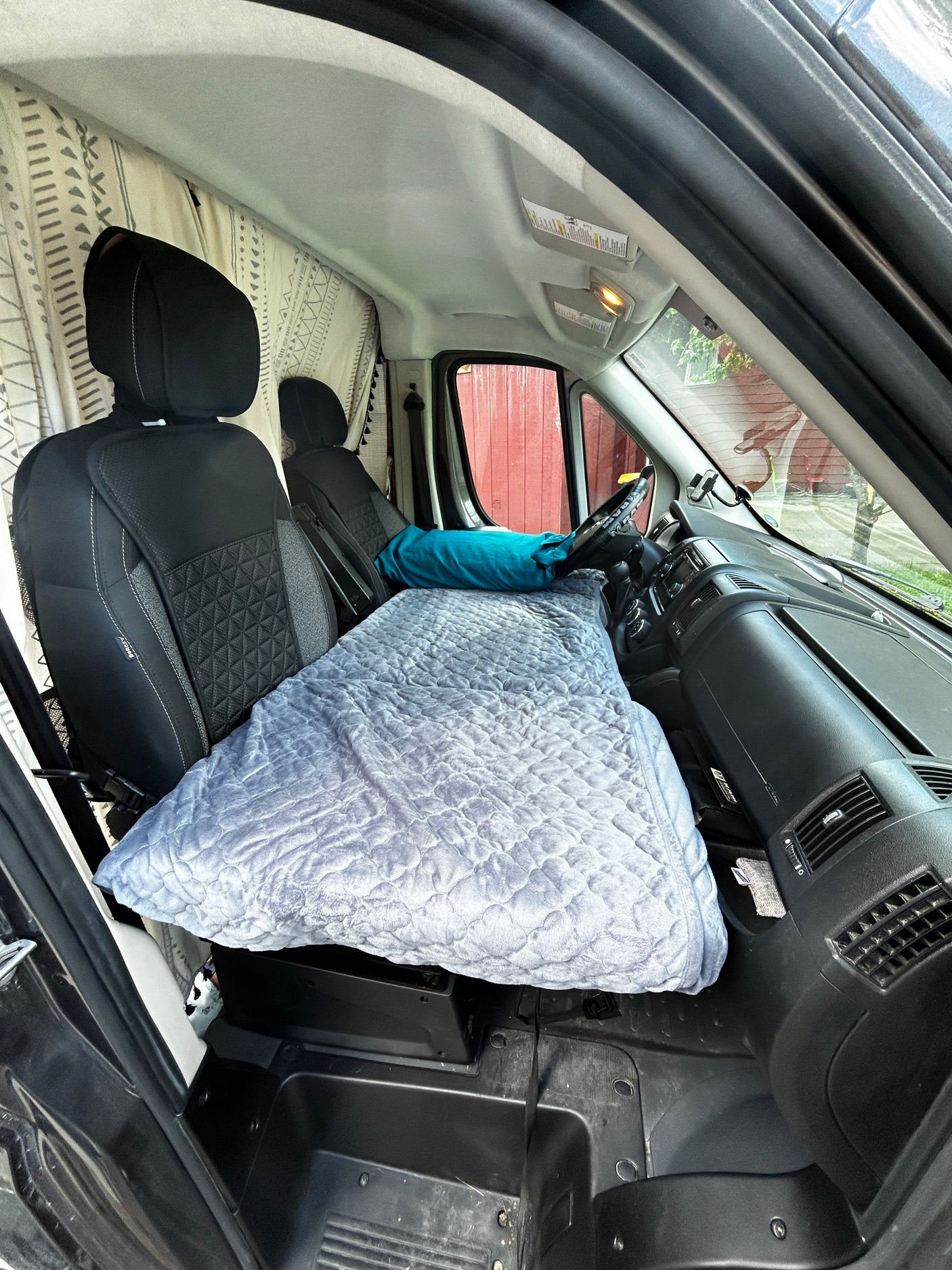 RV rental: Front cabin transformed into a cozy sleeping area. Grey quilted bed extends from seats to dashboard for van travel.