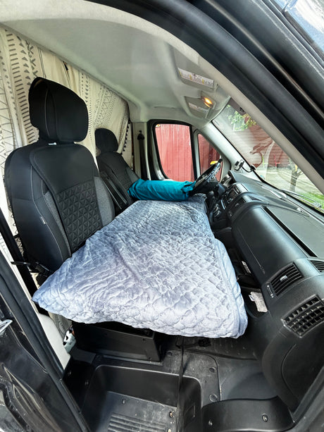 RV rental: Front cabin transformed into a cozy sleeping area. Grey quilted bed extends from seats to dashboard for van travel.