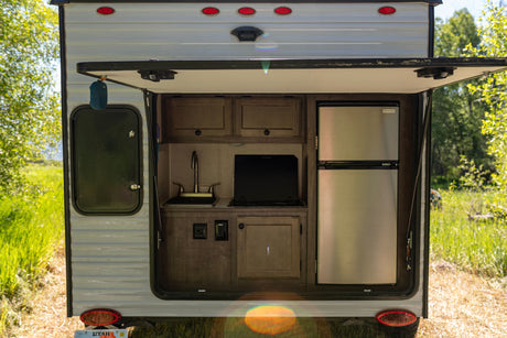 This RV rental features an outdoor kitchen with a sink, stove, and refrigerator, visible through the open rear hatch.