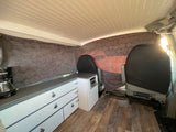 RV rental interior features a compact kitchen with cabinets, beadboard ceiling, and patterned fabric walls. Ideal for travel.