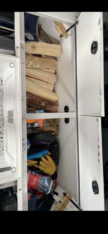 Organized RV rental cabinet with firewood, work gloves, and essential supplies for travel, neatly stowed on shelves.