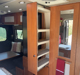 Inside an RV rental: a pull-out pantry with shelves, mirrored door with towel bar, and a dining area by a window.