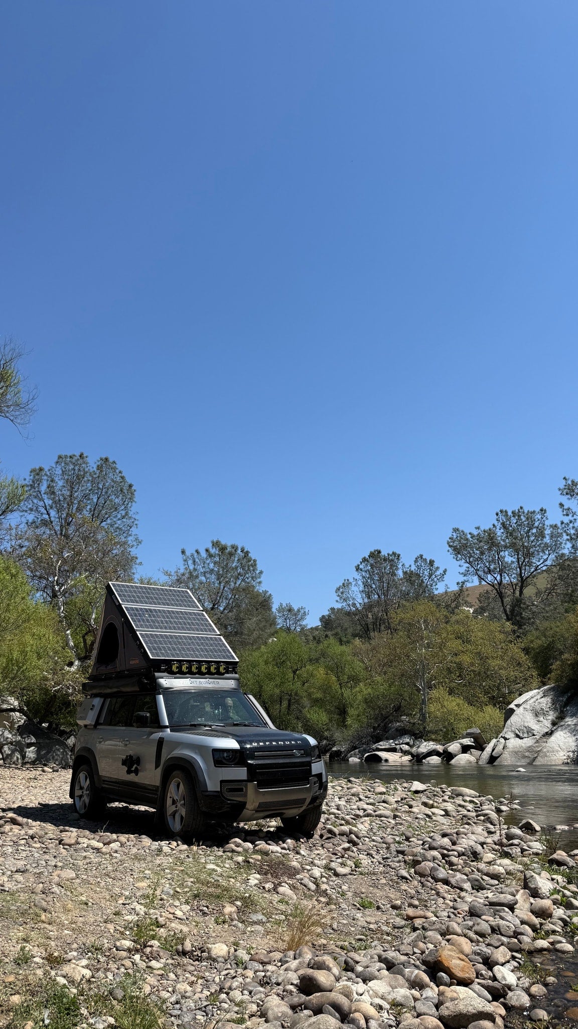 Adventure-ready Land Rover Defender with solar rooftop tent, ideal for an RV rental trip by the river. Perfect for off-grid camping. — photo 10
