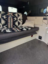 Cozy RV rental interior with patterned blanket, pillow, and portable fans. Ideal for travel.
