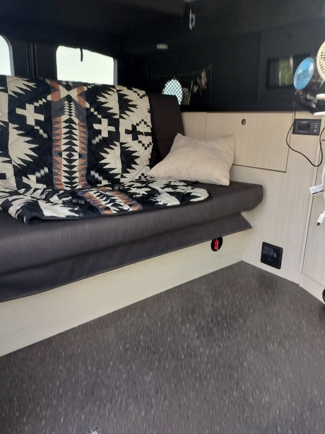 Cozy RV rental interior with patterned blanket, pillow, and portable fans. Ideal for travel.