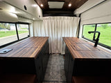 RV rental: Sleek camper van interior features wood counters, black cabinets, and privacy curtain.