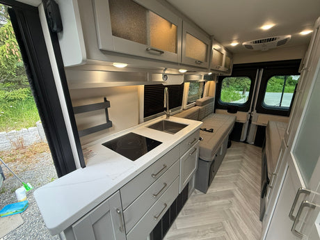 Modern RV rental interior with a bright kitchen, induction cooktop, sink, light gray cabinets, and convertible bed.