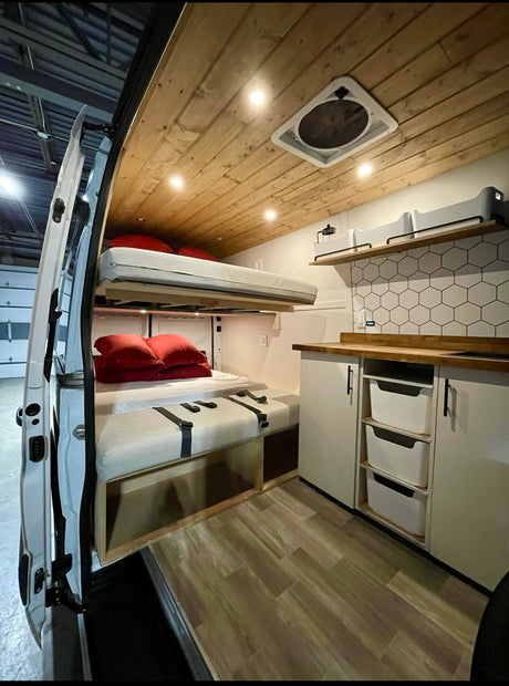 Modern rv rental interior featuring bunk beds, a wood ceiling with fan, organized kitchen, and ample storage.