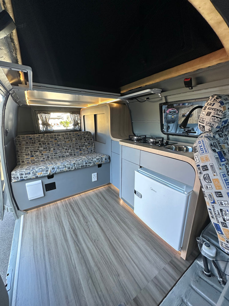 Modern camper van interior for your next rv rental, with a compact kitchen, fridge, comfortable seating, and wood flooring. — photo 8