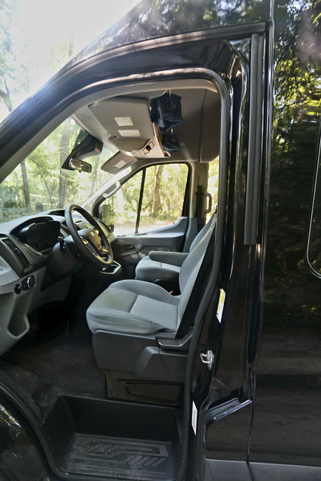 Open door view of an RV rental van's interior: driver's seat, steering wheel, dashboard, and passenger seat.