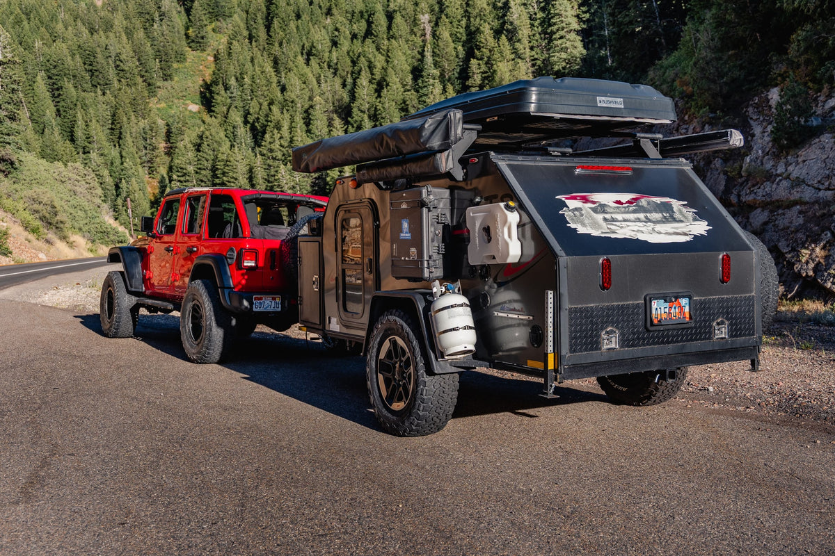 Red Jeep towing a fully-equipped overland RV rental trailer with rooftop tent on a mountain road for camping. — photo 12