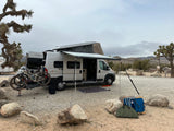 RV rental with bikes & pop-top awning extended, ready for desert camping among Joshua trees.