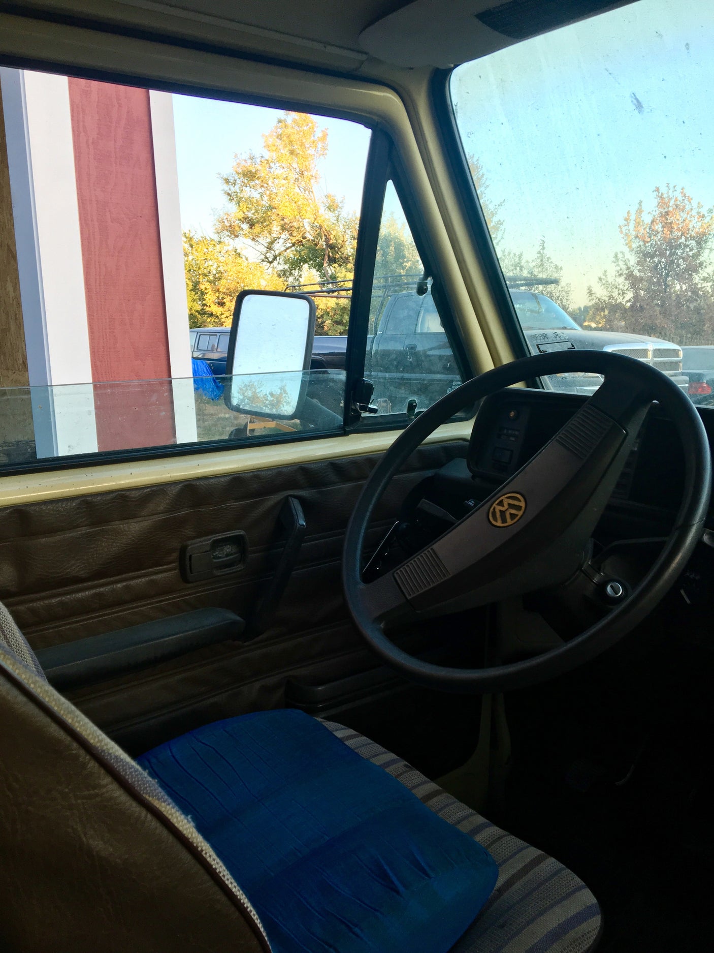 Driver's view from an RV rental, featuring steering wheel, dashboard, and autumn outdoor scenery including a barn.