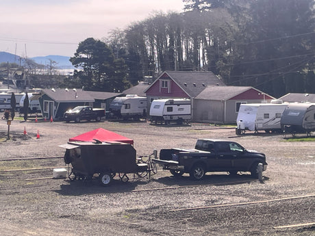 RV rental facility: Pickup truck towing a camping trailer with a red canopy, parked among various RVs and buildings.