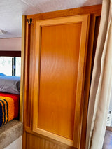 RV rental interior featuring a wooden cabinet door with a storage hook, offering practical storage solutions next to a bed.