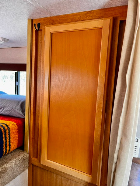 RV rental interior featuring a wooden cabinet door with a storage hook, offering practical storage solutions next to a bed.