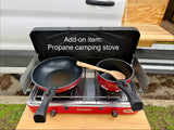 RV rental add-on: Red propane camping stove with pan and pot on a wooden table, ready for outdoor cooking.