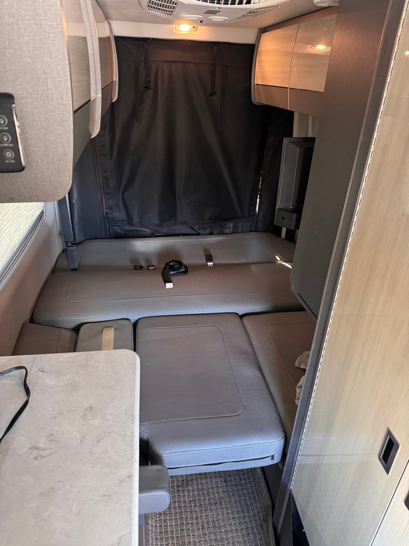 RV rental interior: versatile grey seating converts to a bed, with a black privacy curtain and storage cabinets. — photo 9