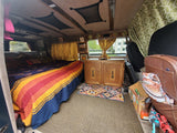 Cozy RV rental interior with a bed, wooden cabinet, and clever storage solutions, ideal for adventurous travel.