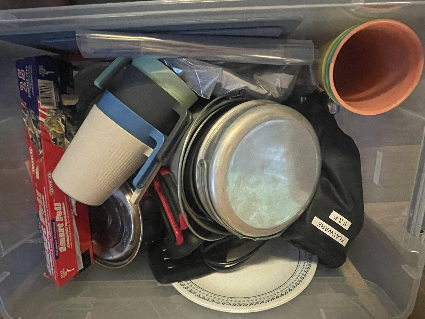 RV rental kitchen kit: foil, mugs, pots, flatware, & plates packed for convenience in a clear bin.