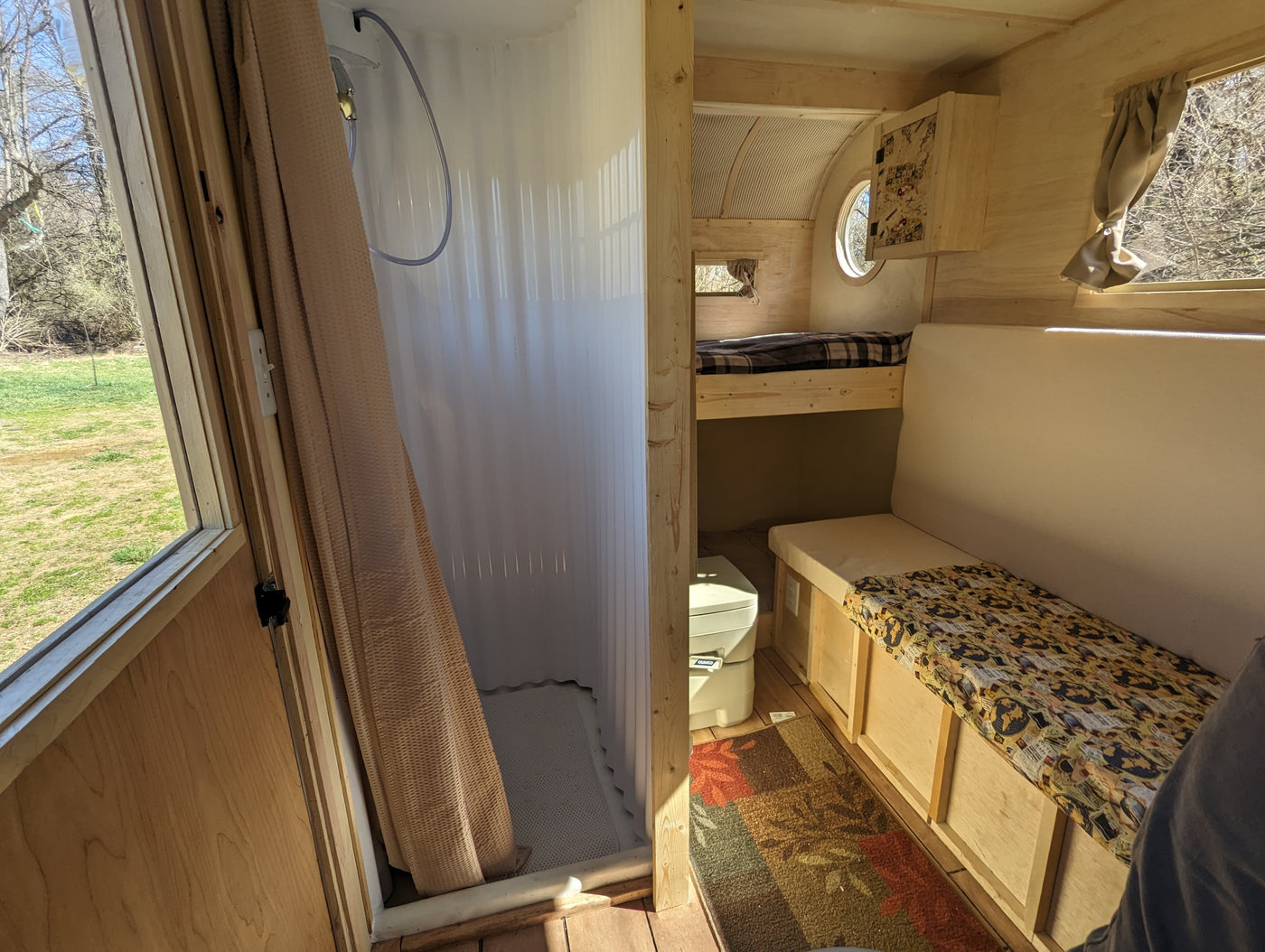 RV rental interior: cozy wooden camper with a shower, bunk bed, dinette seating, and portable toilet. Outdoor view from windows. — photo 4