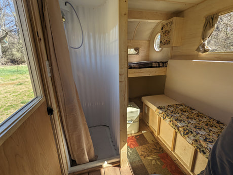 RV rental interior: cozy wooden camper with a shower, bunk bed, dinette seating, and portable toilet. Outdoor view from windows.