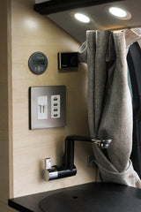 An RV rental's cozy interior features: a Victron battery monitor (13.2V), Webasto, USB charging, outlet, faucet, and curtain.