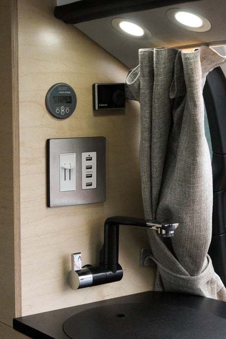 An RV rental's cozy interior features: a Victron battery monitor (13.2V), Webasto, USB charging, outlet, faucet, and curtain.