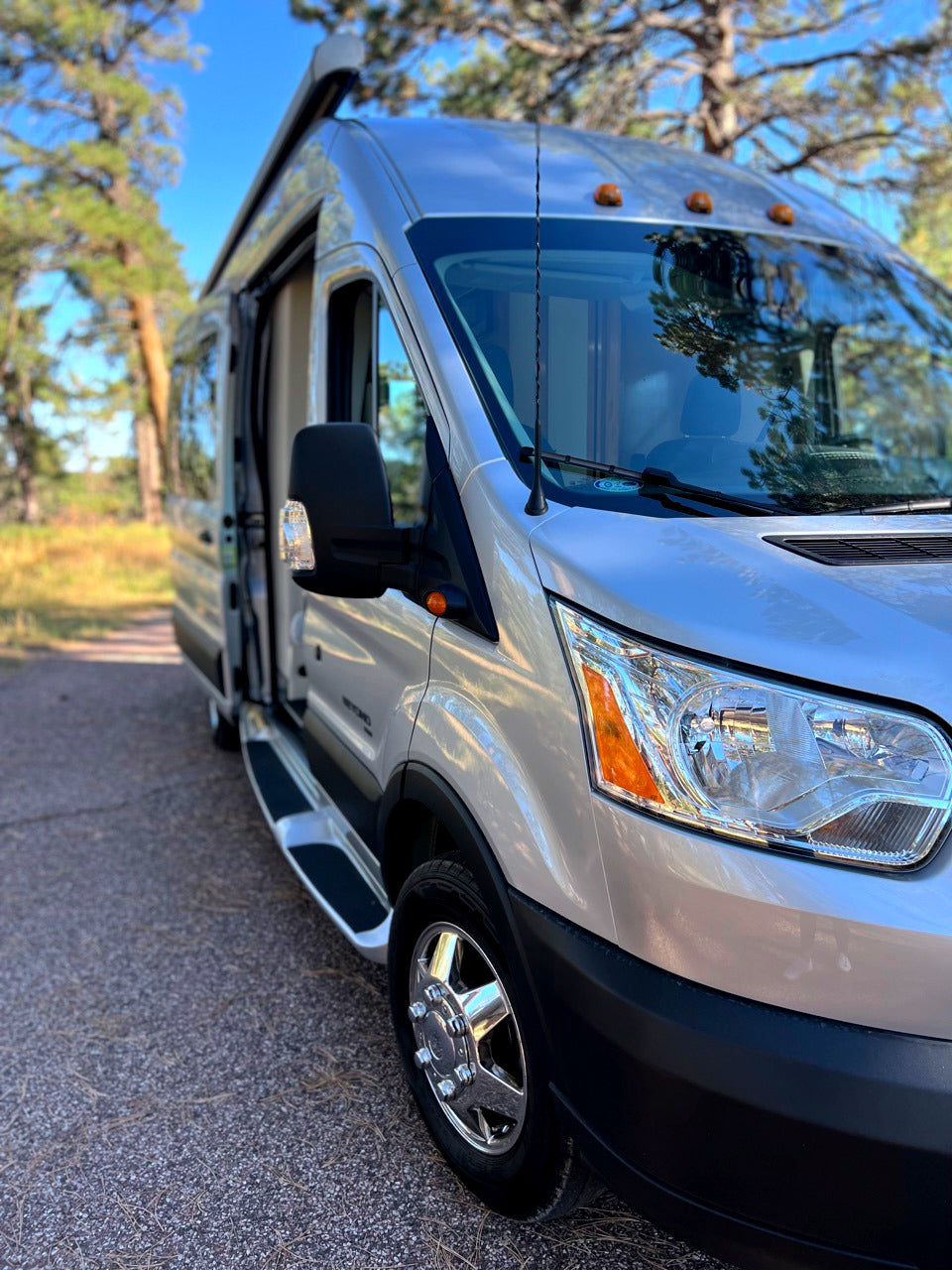 This silver camper van, ideal for RV rental adventures, is parked outdoors with its side door open, ready for travel.
