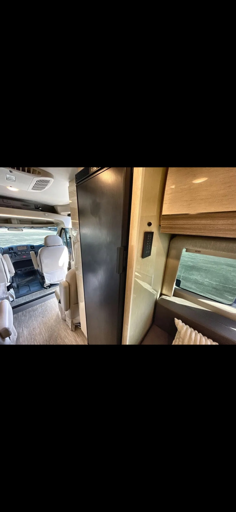 Modern RV rental interior: view of beige seating, dark fridge, and side wall controls. Ideal for your next road trip. — photo 4
