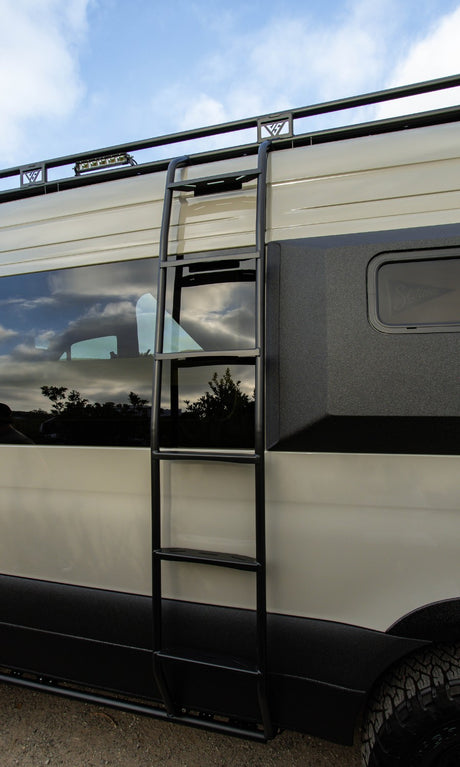 Close-up of a custom RV rental van, featuring a roof rack, sturdy access ladder, and rugged two-tone exterior.