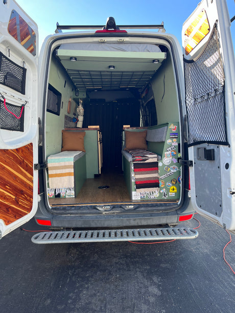 Rear view of a custom green camper van interior, ideal for an RV rental, with cozy benches and an upper bed.