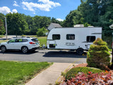 White SUV towing a modern RV rental travel trailer, parked on a sunny suburban driveway, ready for adventure.
