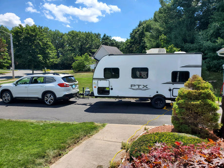 White SUV towing a modern RV rental travel trailer, parked on a sunny suburban driveway, ready for adventure.