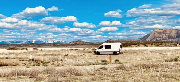 White RV rental parked in a vast dry field with distant snow-capped mountains under a blue, cloudy sky.