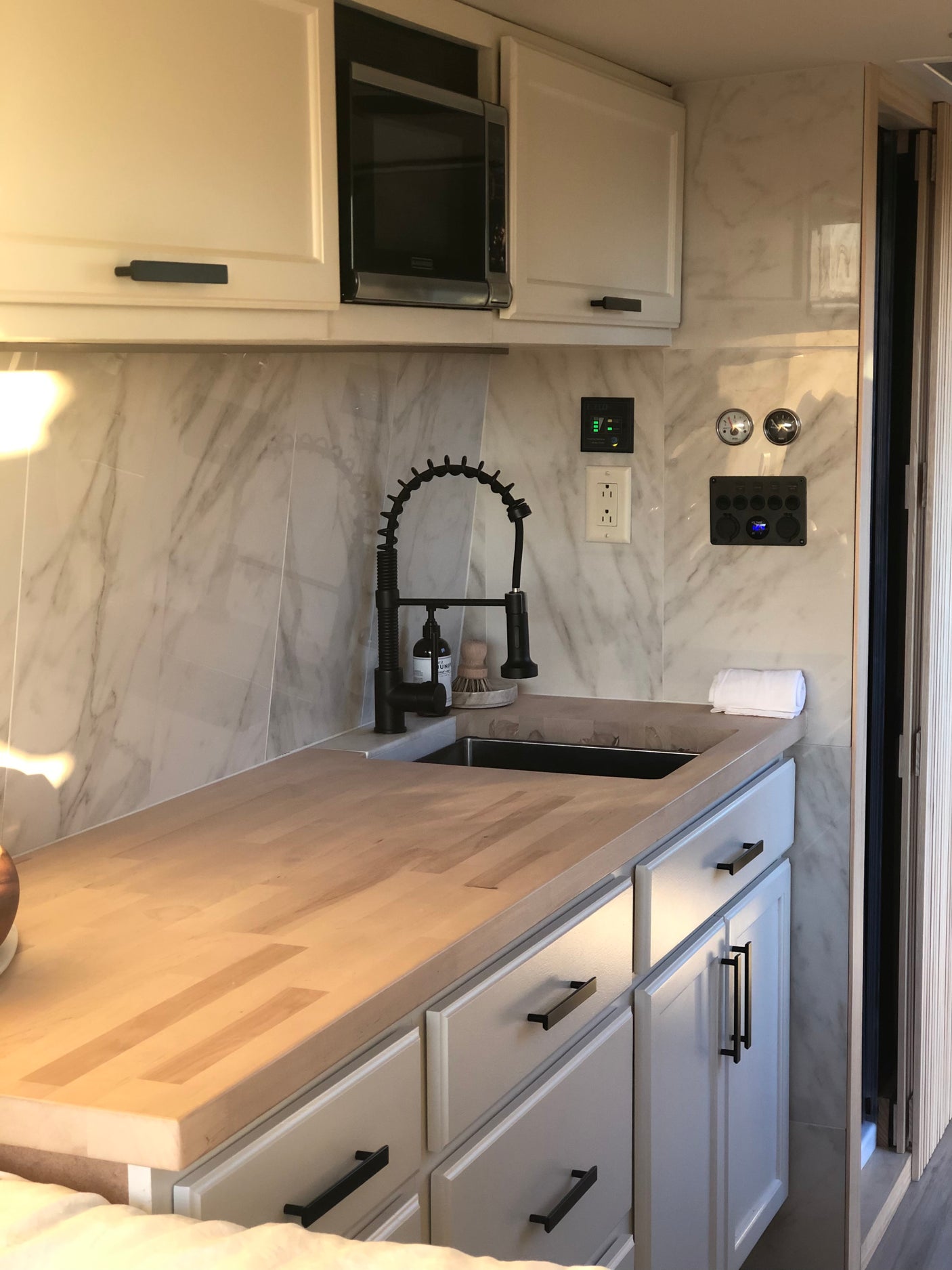 Modern RV rental kitchen with white cabinets, black hardware, microwave, light wood countertops, and a sleek black sink faucet.