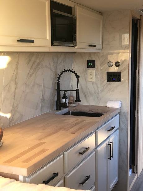 Modern RV rental kitchen with white cabinets, black hardware, microwave, light wood countertops, and a sleek black sink faucet.
