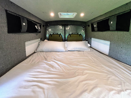 This RV rental's cozy interior features a large bed, integrated storage, and blinds for privacy.