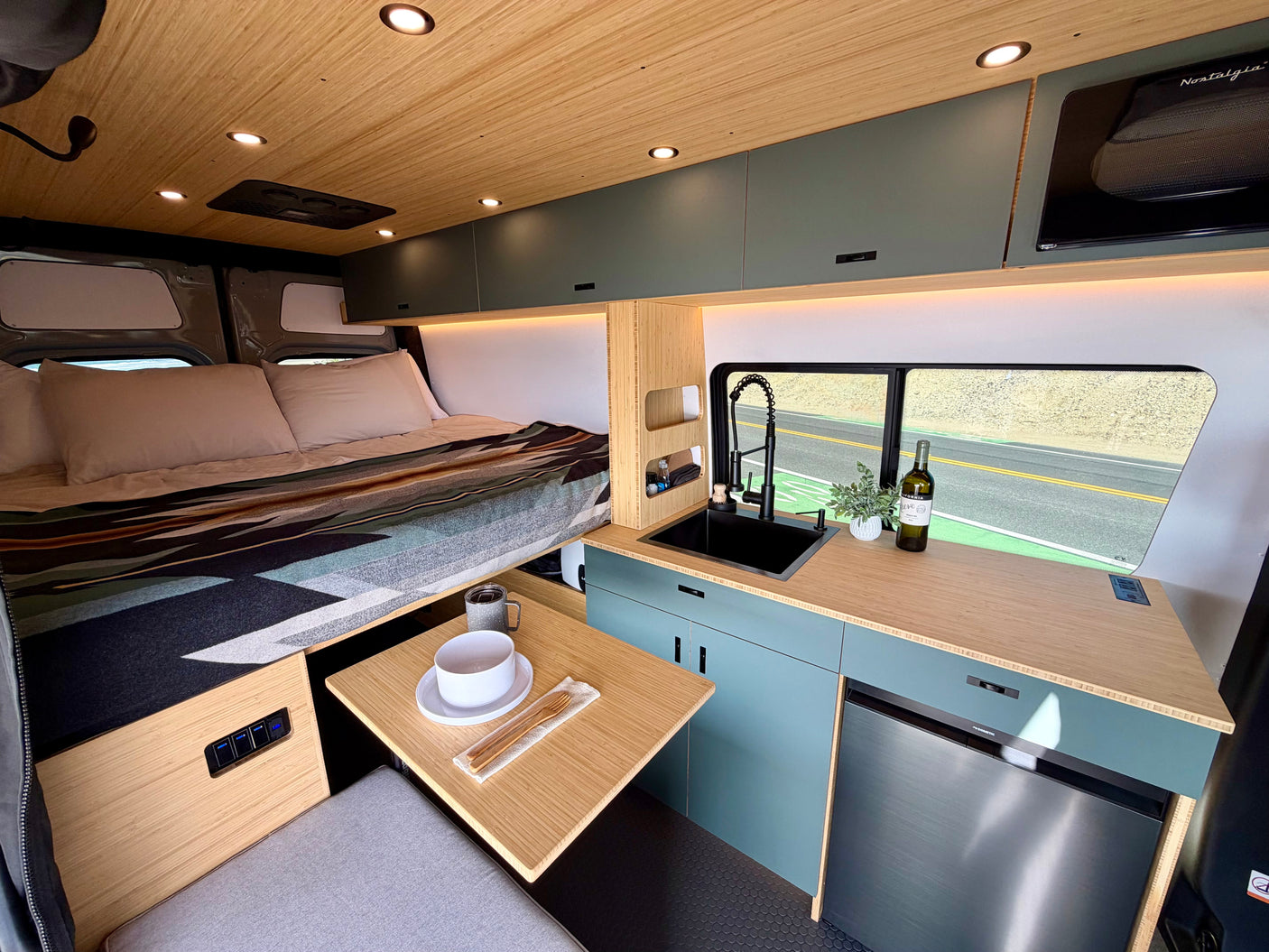 Experience comfort in this modern rv rental camper van interior. Features a cozy bed, compact kitchen, & scenic road views.