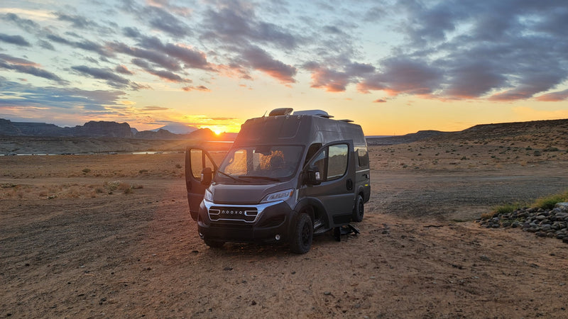 This RV rental camper van is parked on a dirt road at sunset, with warm light, clouds, mountains, and a lake in the background. — photo 10
