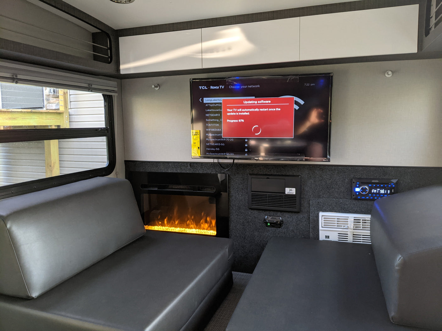 This RV rental interior features a smart TV updating software (67%), a glowing electric fireplace, comfy black seating, and overhead cabinets.