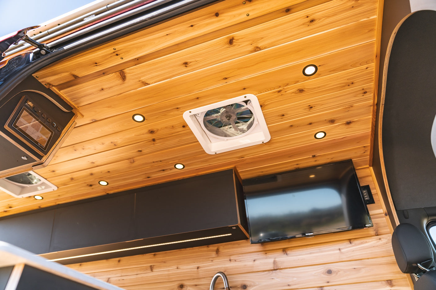 Luxury RV rental interior: cedar paneling, ceiling fan, recessed lights, microwave, TV, sleek cabinets, and accent lighting.